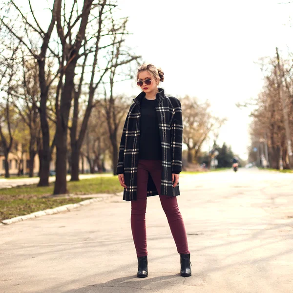 Beautiful girl in plaid coat and sunglasses standing on a strree — Stock Photo, Image