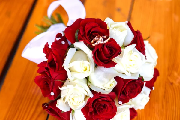 Dva snubní prsteny v kytici červených a bílých růží na dřevěný — Stock fotografie