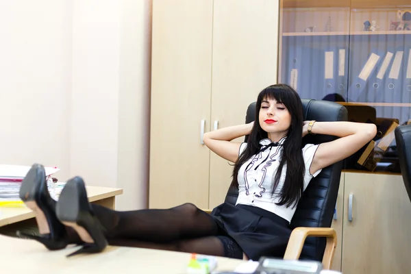 Hermosa mujer se acuesta en una oficina en un escritorio con las piernas en — Foto de Stock