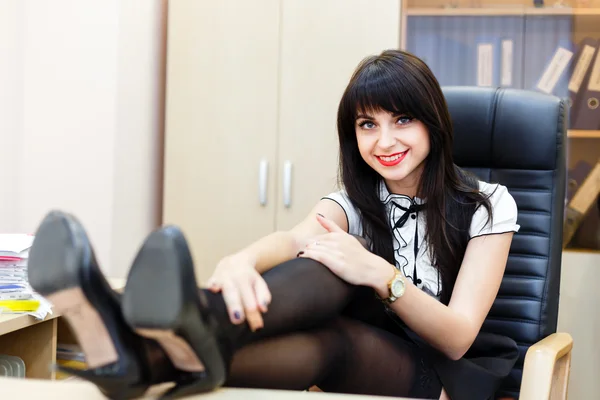 Gülümseyen bir ofiste th bacaklarına ile bir masada oturan kadın — Stok fotoğraf