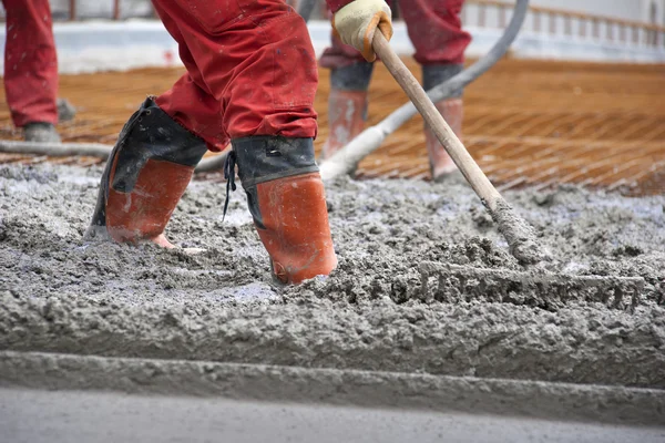 Arbeiter in roten Stiefeln mit Harke ebneten den Beton — Stockfoto