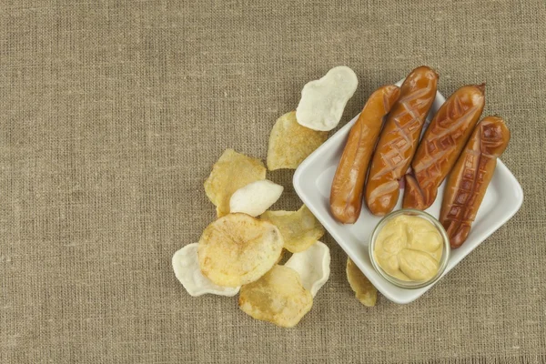 Grilled Sausage and potato chips on linen tablecloth. — Stock Photo, Image