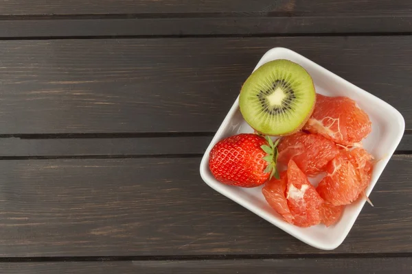 Programa de dieta, comida cruda. Kiwi, fresa y pomelo rojo en un plato de porcelana. Alimento lleno de vitaminas . —  Fotos de Stock