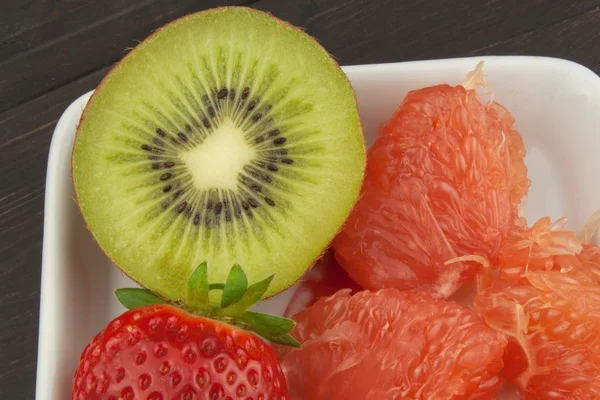 Programa de dieta, comida cruda. Kiwi, fresa y pomelo rojo en un plato de porcelana. Alimento lleno de vitaminas . —  Fotos de Stock