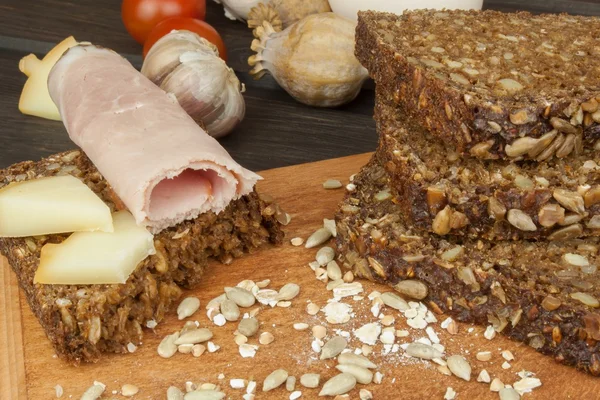 Jambon, fromage et pain de blé entier. Pain de blé entier fraîchement cuit. Préparation du petit déjeuner fait maison. Divers ingrédients pour le repas. Pain tranché sur planche à découper. Publicité sur la boulangerie . — Photo