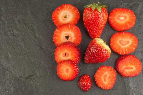 Färska jordgubbar på en svart skiffer bakgrund. Dekoration av skivade jordgubbar. Att göra diet. — Stockfoto
