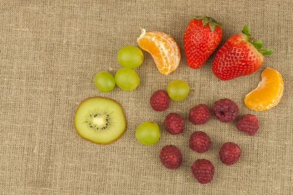 Frambuesa, fresa, mandarina, uvas y kiwi sobre fondo de lona. Comida saludable en la mesa de la cocina. Preparación de frutero . —  Fotos de Stock