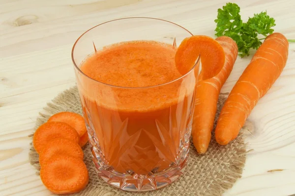 Glass of carrot juice and carrots on the wooden table. Healthy juice full of vitamins and fiber. Diet Food. Carrot segments on a wooden background. — Stock Photo, Image