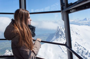 Beautiful girl in the cabin of the cable car, high above the mountains. View from the gondola. A young girl on vacation in the mountains.