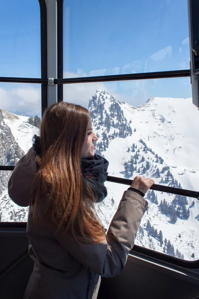 Beautiful girl in the cabin of the cable car, high above the mountains. View from the gondola. A young girl on vacation in the mountains. — Stock Photo, Image