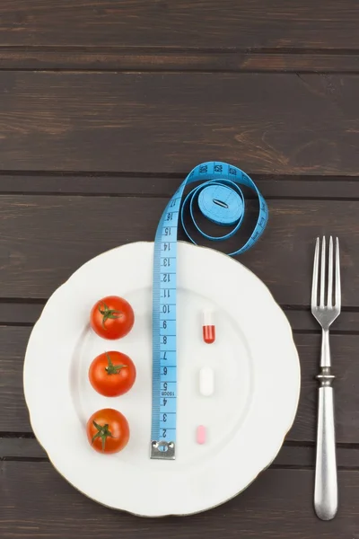 Dieta e suplementos em uma mesa de madeira. Refeições dietéticas rigorosas. Dieta de emagrecimento. Tomates e comprimidos . — Fotografia de Stock