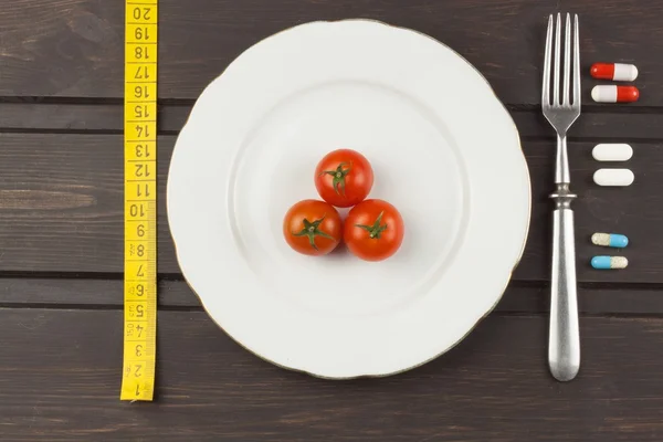 Dieta e suplementos em uma mesa de madeira. Refeições dietéticas rigorosas. Dieta de emagrecimento. Tomates e comprimidos . — Fotografia de Stock