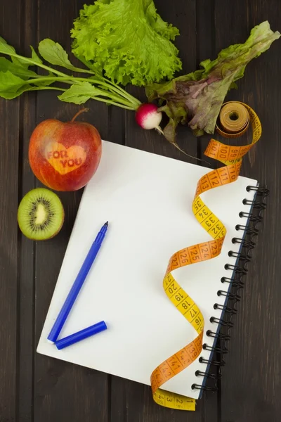 Preparing for the diet program. The decision to initiate dieting. Planning of diet. Notebook measuring tapes and pen on wooden table.