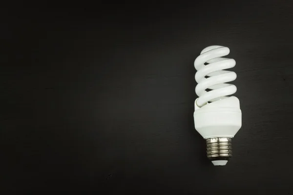 Energisparande lampa på svart trä bakgrund. Försäljning av glödlampor. Reklam för energisparande glödlampor. Plats för din text. — Stockfoto