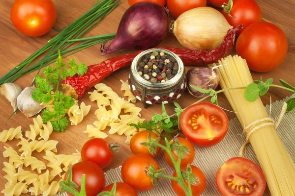 生的意大利面，在木制背景上用西红柿和欧芹。准备饮食食品。简单晚餐的食谱。传统意大利面与蔬菜. — 图库照片