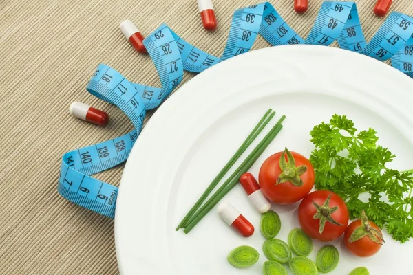 Strenge Diät gegen Fettleibigkeit. pflanzliche Kost. Tomaten auf einem Teller. Rohes Gemüse auf weißem Teller und Maßband. — Stockfoto