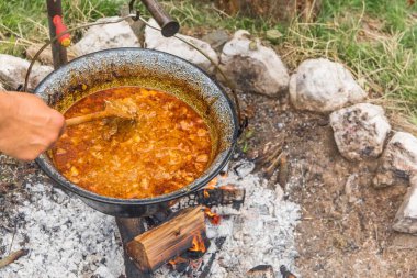 Şenlik ateşinde kaynayan metal kazan. Açık ateşte yemek pişirmek, kamp yapmak. Kamp ateşinde geleneksel gulaş hazırlığı.