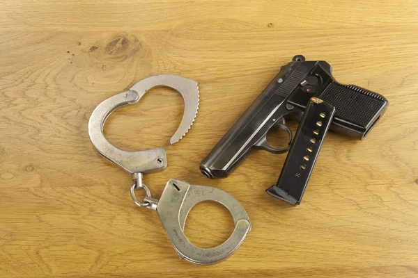 Skjutvapen liggande på bordet, metal polis handbojor — Stockfoto