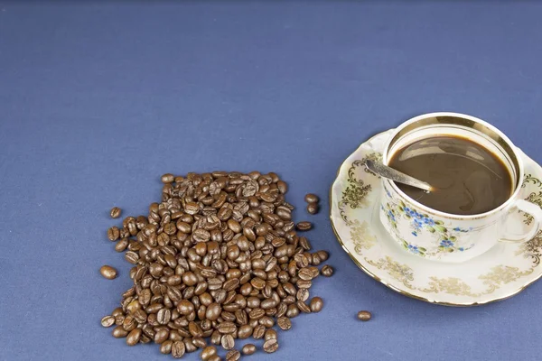 Кофейная кружка на столе с голубой скатертью, вылитой из кофейных зерен — стоковое фото