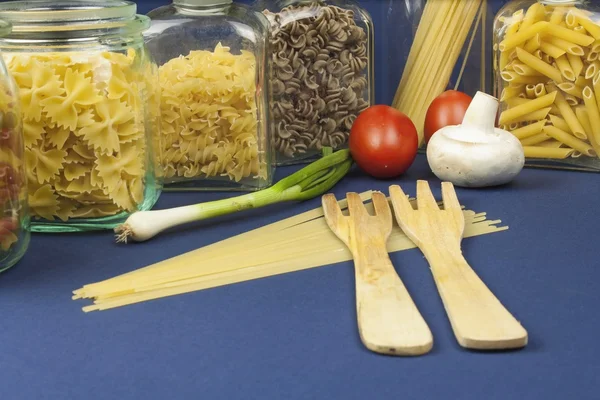 Diferentes tipos de pasta sobre la mesa, junto con verduras, listas para cocinar — Foto de Stock