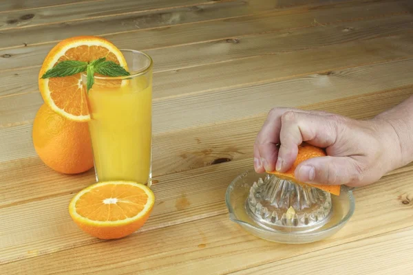 A hand squeezing juice from an orange on a manual glass squeezer. Set on a wooden planked table. Domestic production of orange juice.
