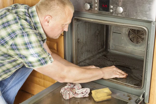 adam mutfakta yerde diz çöker ve fırın temizler. Temizlik çalışmaları içinde belgili tanımlık ev. Adam karısını hizmetçi servisi ile yardım.