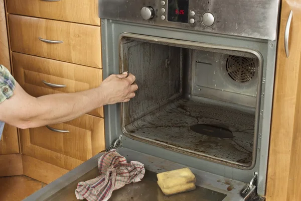 El hombre se arrodilla en el suelo de la cocina y limpia el horno. Trabajos de limpieza en el hogar. Hombre ayudando a su esposa con el servicio de limpieza . —  Fotos de Stock