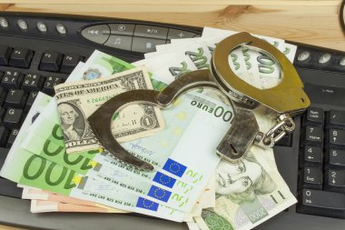 The concept of cybercrime. Criminal activity performed by computers and the Internet. Valid banknotes euro and the Czech koruna. Arrest cybercriminals, metal handcuffs and computer keyboard.