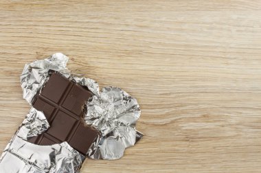 Alüminyum folyo bir ahşap tahta üzerinde çikolata sarılı. Kaydırılan tatlı tedavi.