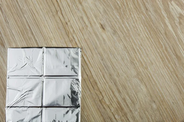 Chocolate wrapped in aluminum foil on a wooden board. Wrapped sweet treat. — Stock Photo, Image