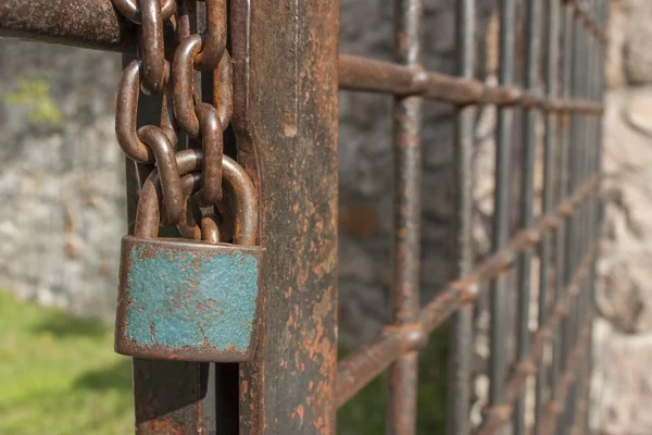 De vergrendeling van de keten. Oude roestige ketting met een slot op de ijzeren poort. Symbool gevangenisstraf en slavernij. Eigenschap beveiligingsketen. Gesloten ijzeren poort met een slot. — Stockfoto