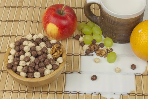 Spilled milk on the kitchen table. Chocolate cereal balls in a bowl of bamboo. Healthy breakfast with fruit and milk. A diet full of energy and fiber for athletes. Quick to prepare homemade breakfast. — Stockfoto
