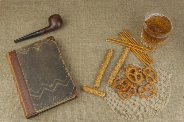 Cerveza en un vaso y un libro sobre la mesa. Paja de trigo crujiente con sal. Montón de palitos de pretzel. Entretenimiento para ver TV . —  Fotos de Stock