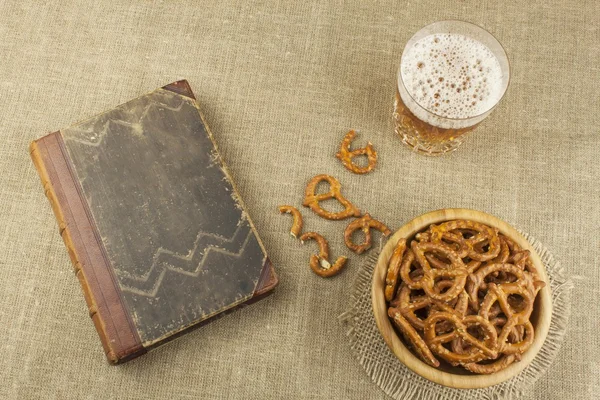 Cerveza en un vaso y un libro sobre la mesa. Paja de trigo crujiente con sal. Montón de palitos de pretzel. Entretenimiento para ver TV . — Foto de Stock