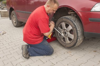 Man changing the punctured tyre on his car loosening the nuts with a wheel spanner before jacking up the vehicle. Repair flat tire on a passenger car. Replacing summer tires for winter tires.