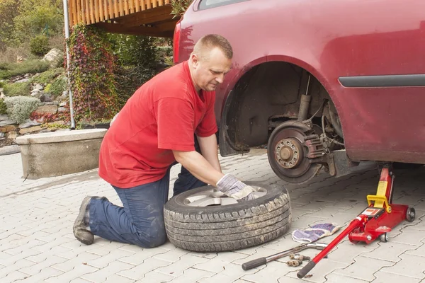 Der Mann wechselte den zerstochenen Reifen an seinem Auto und löste die Muttern mit einem Radschlüssel, bevor er das Fahrzeug aufbockte. Reifenplatzer an einem PKW reparieren. Sommerreifen gegen Winterreifen austauschen. — Stockfoto