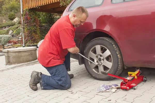 Der Mann wechselte den zerstochenen Reifen an seinem Auto und löste die Muttern mit einem Radschlüssel, bevor er das Fahrzeug aufbockte. Reifenplatzer an einem PKW reparieren. Sommerreifen gegen Winterreifen austauschen. — Stockfoto