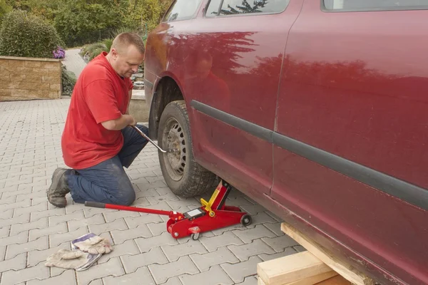 Der Mann wechselte den zerstochenen Reifen an seinem Auto und löste die Muttern mit einem Radschlüssel, bevor er das Fahrzeug aufbockte. Reifenplatzer an einem PKW reparieren. Sommerreifen gegen Winterreifen austauschen. — Stockfoto