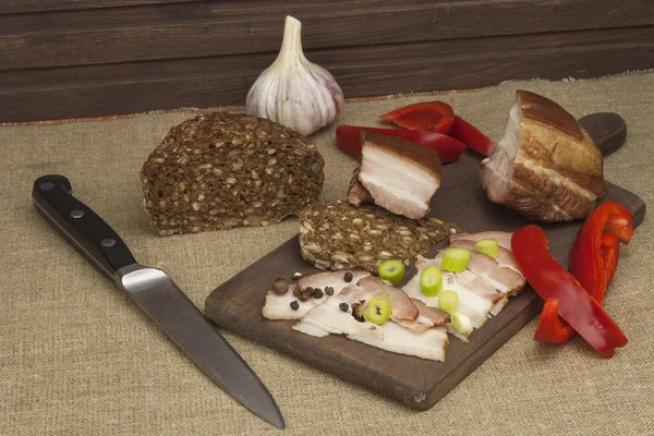 Preparing home-made snacks for the guests. Cutting board with smoked bacon and bread. Raw bacon. Whole grain bread.