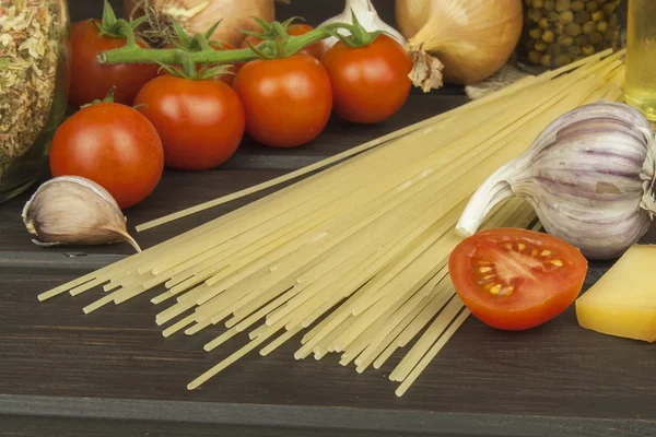 Preparación de pasta casera. Pasta y verduras en una mesa de madera. Alimento dietético. Pastas, tomates, cebolla, aceite de oliva y albahaca sobre fondo de madera . — Foto de Stock