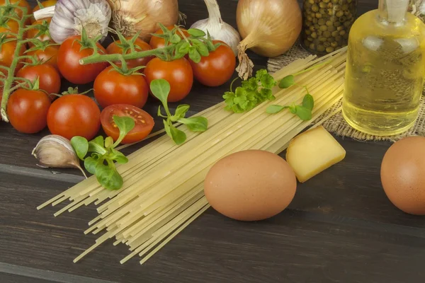 准备自制意大利面。意大利面和蔬菜木制的桌子上。饮食的食品。意大利面、 西红柿、 洋葱、 橄榄油、 罗勒木背景. — 图库照片