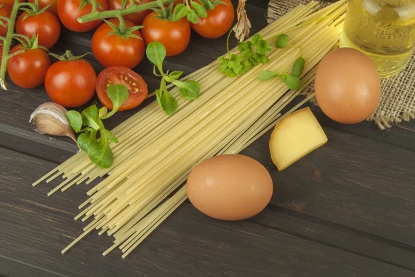 Förbereda hemlagad pasta. Pasta och grönsaker på ett träbord. Dietary mat. Pasta, tomater, lök, olivolja och basilika på trä bakgrund. — Stockfoto