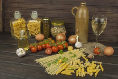 Bir bardak şarap ve makarna. Ev yapımı makarna hazırlanıyor. Makarna ve sebzeler üzerinde ahşap bir masa. Diyet yiyecek. Makarna, domates, soğan, zeytin yağı ve fesleğen ahşap arka plan üzerinde.