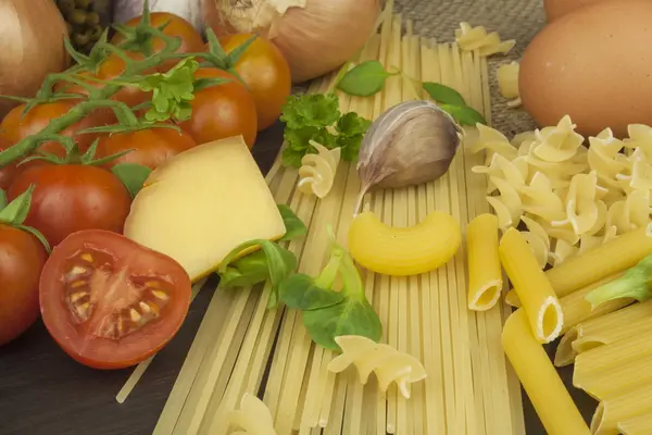 Pasta y verduras en una mesa de madera. Alimento dietético. Pastas, tomates, cebolla, aceite de oliva y albahaca sobre fondo de madera . — Foto de Stock