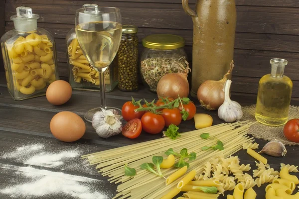 Copo de vinho e massa. A preparar massa caseira. Macarrão e legumes em uma mesa de madeira. Comida dietética. Massas, tomates, cebola, azeite e manjericão sobre fundo de madeira . — Fotografia de Stock