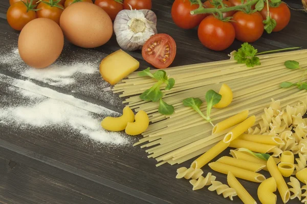 Spilld mjöl. Pasta och grönsaker på ett träbord. Dietary mat. Pasta, tomater, lök, olivolja och basilika på trä bakgrund. — Stockfoto