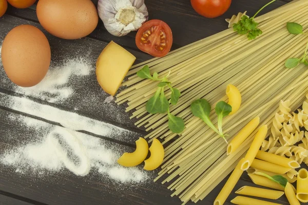 洒了的面粉。意大利面和蔬菜木制的桌子上。饮食的食品。意大利面、 西红柿、 洋葱、 橄榄油、 罗勒木背景. — 图库照片