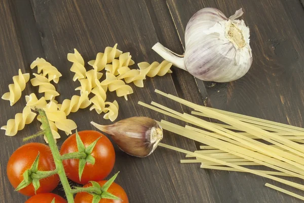 Przygotowanie menu. Makaronu i warzyw na drewnianym stole. Diety żywności. Makaron, pomidory, cebula, oliwa z oliwek i bazylii na drewniane tła. — Zdjęcie stockowe