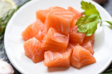 Ham somon fileto küp, siyah arka planda beyaz tabakta otlar ve baharatlar.. 