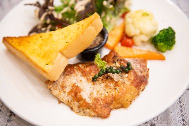 Kızarmış biftek, domuz pirzolası, sebzeli sebze, karabiberli mısır ve yemek masasındaki beyaz tabakta biftek soslu ekmek.